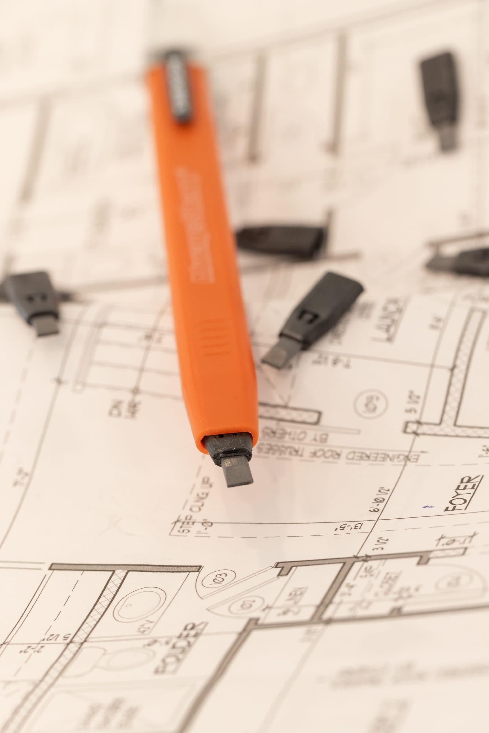 Swanson AlwaysSharp® refillable carpenter pencil standing tip-down on a blueprint with refill cartridges scattered around.