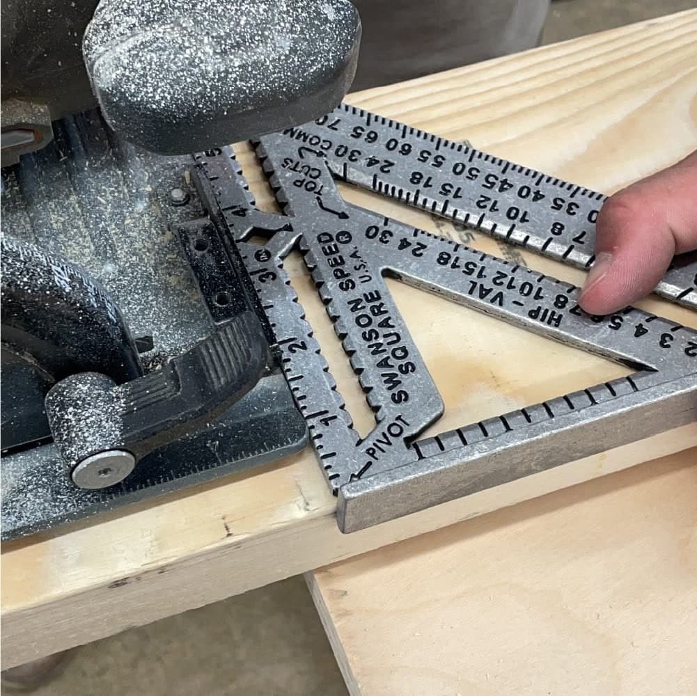 A circular saw making a cut along the long edge of a Swanson Speed® Square PRO held against framing lumber as a saw guide.