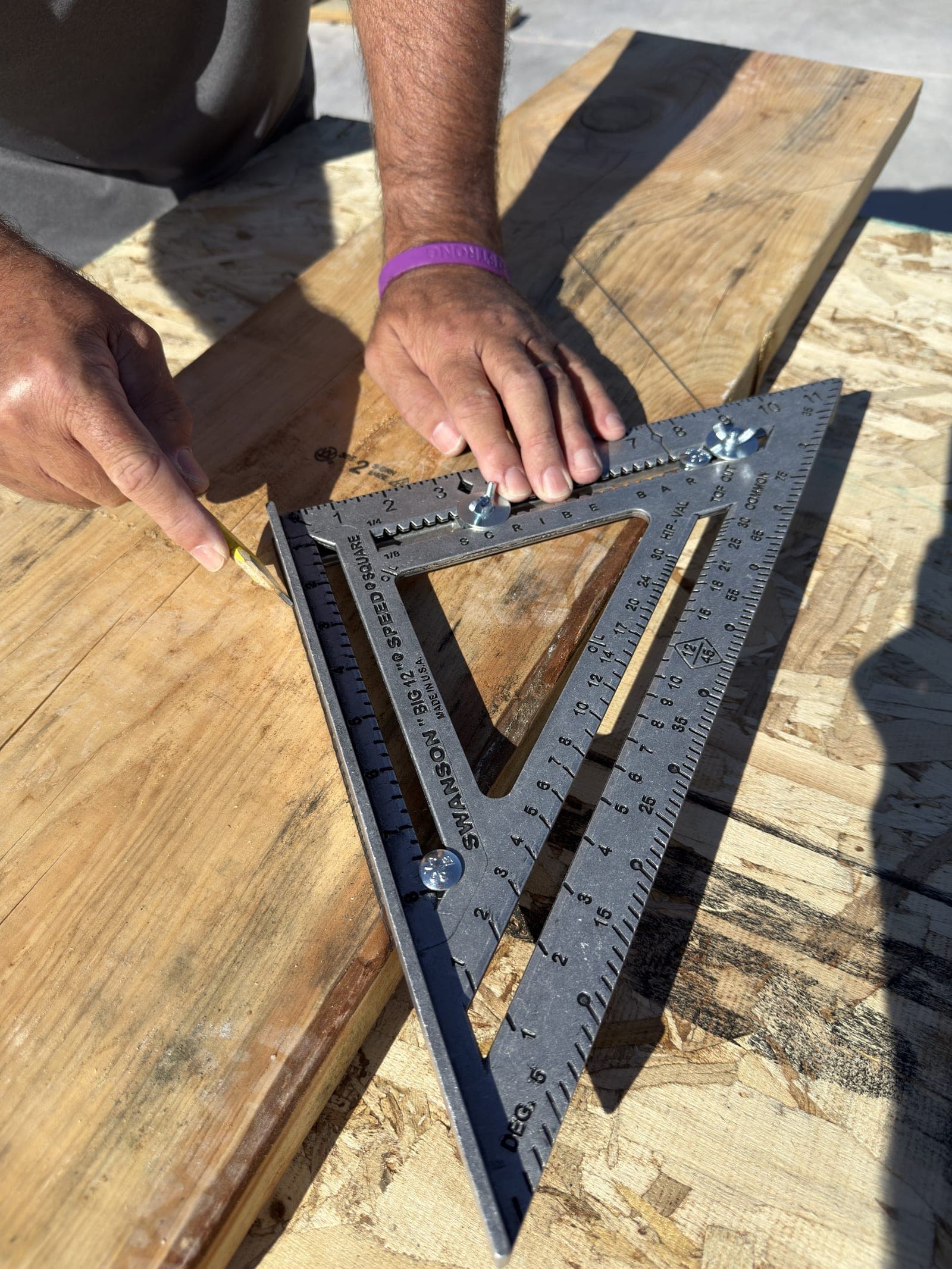 Hands using a Swanson Big 12® Speed® Square on framing lumber on a jobsite.