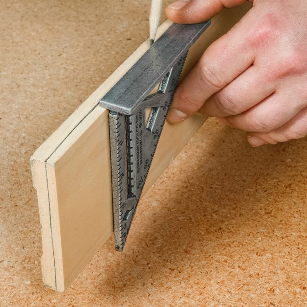 A Swanson Trim Speed® Square hooked over the edge of a piece of stock to scribe a centered mark, showing the dual reference base.