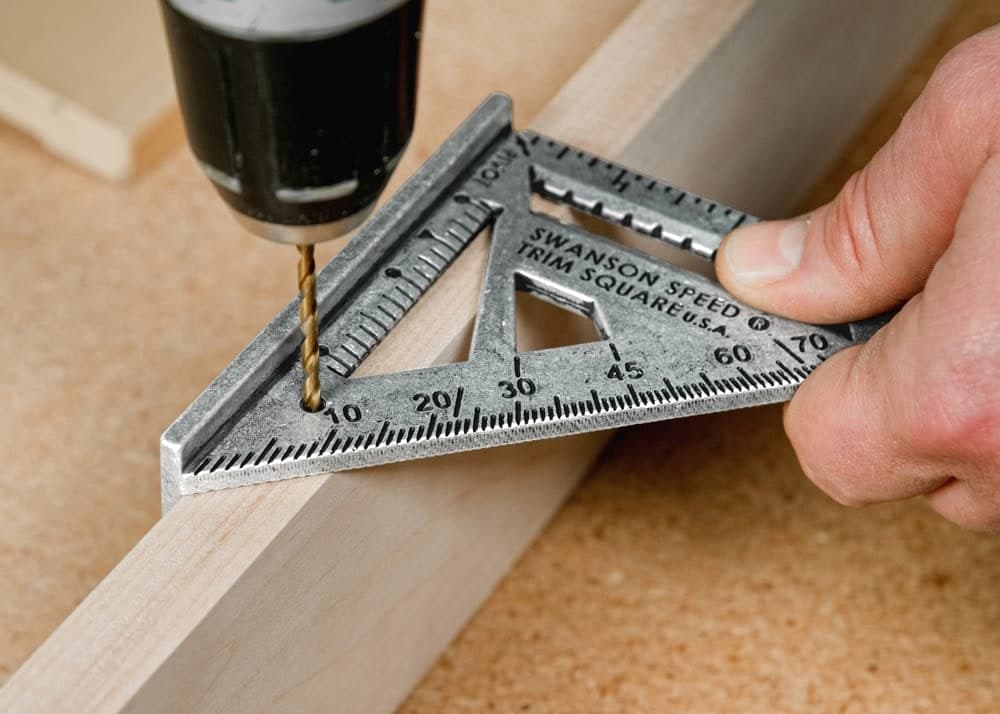 A drill bit going through the 3/8 in. drill-guide hole on a Swanson Trim Speed® Square set on a piece of 3/4 in. stock.